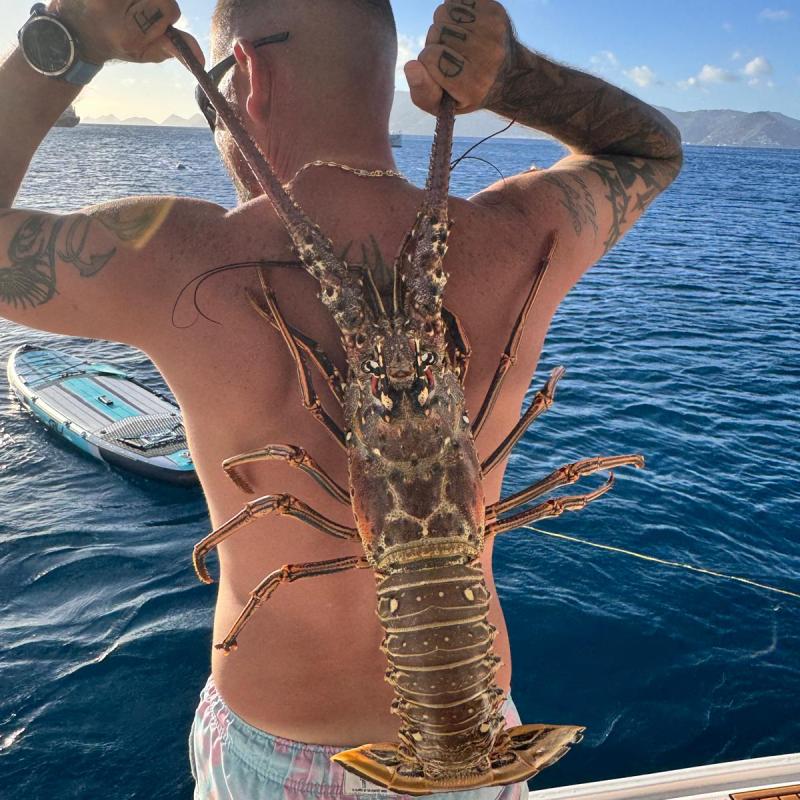 Man holding a large lobster over his shoulder on a boat.