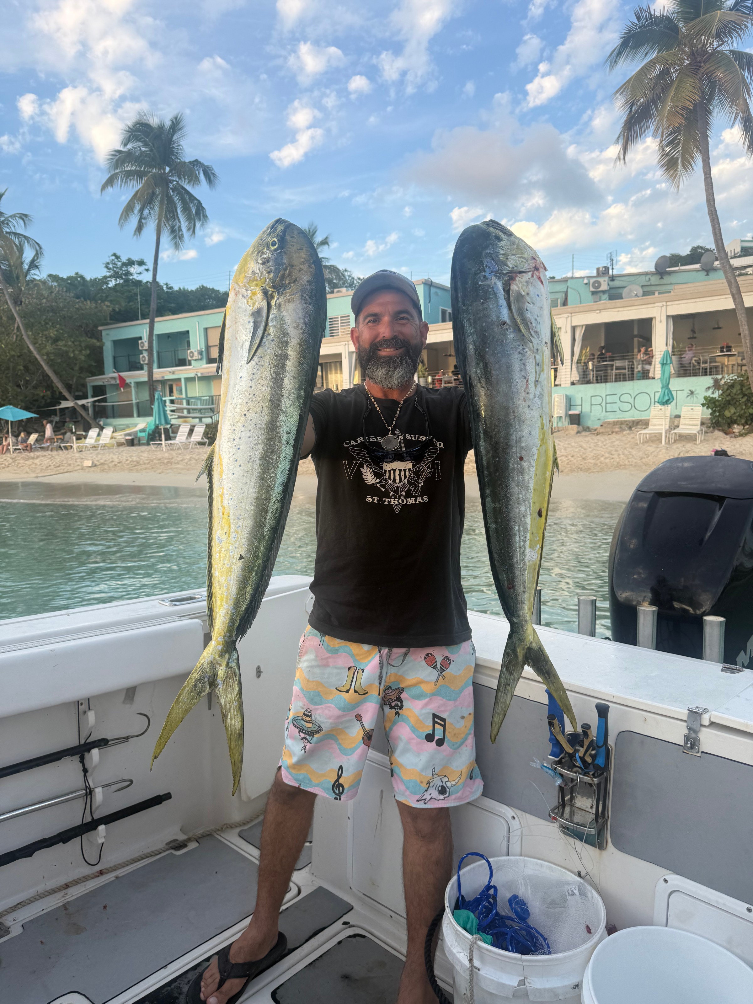 Person holding two large fish on a boat near a beach resort.