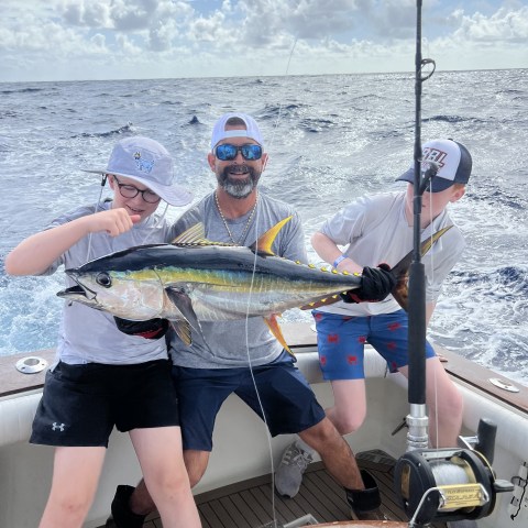 Three people holding a large fish on a boat in the ocean.