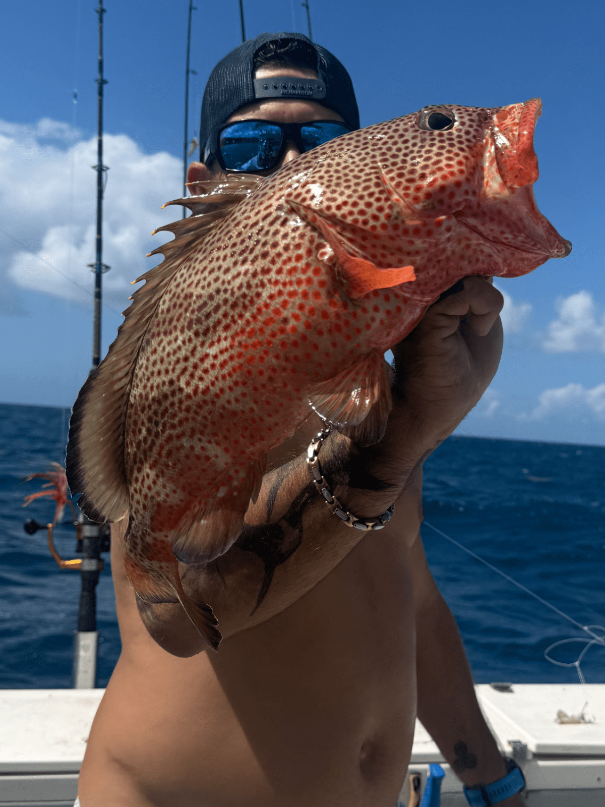 Person holding a large fish on a boat with ocean in background.