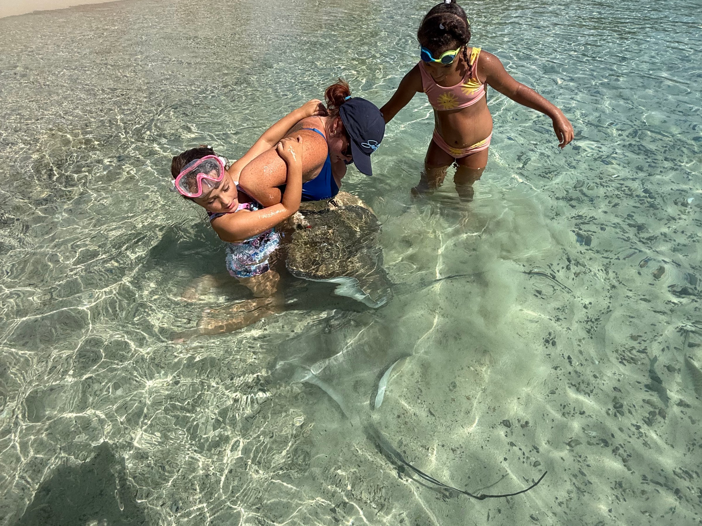 Two women snorkeling in shallow beach water examining a stingray.