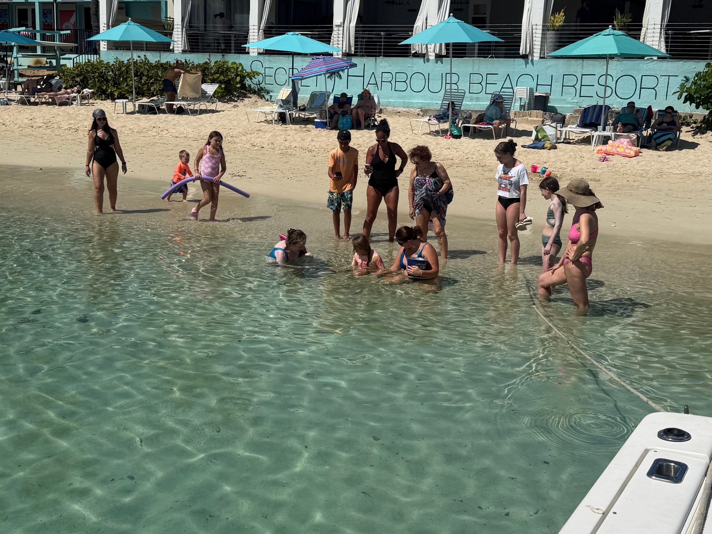 Group of people standing in shallow water on a beach near a resort.