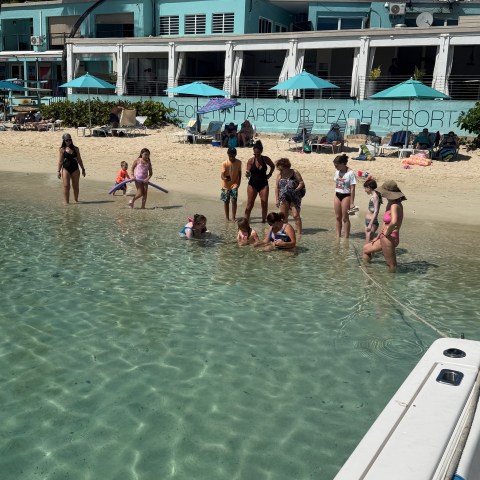 Group of people standing in shallow water on a beach near a resort.