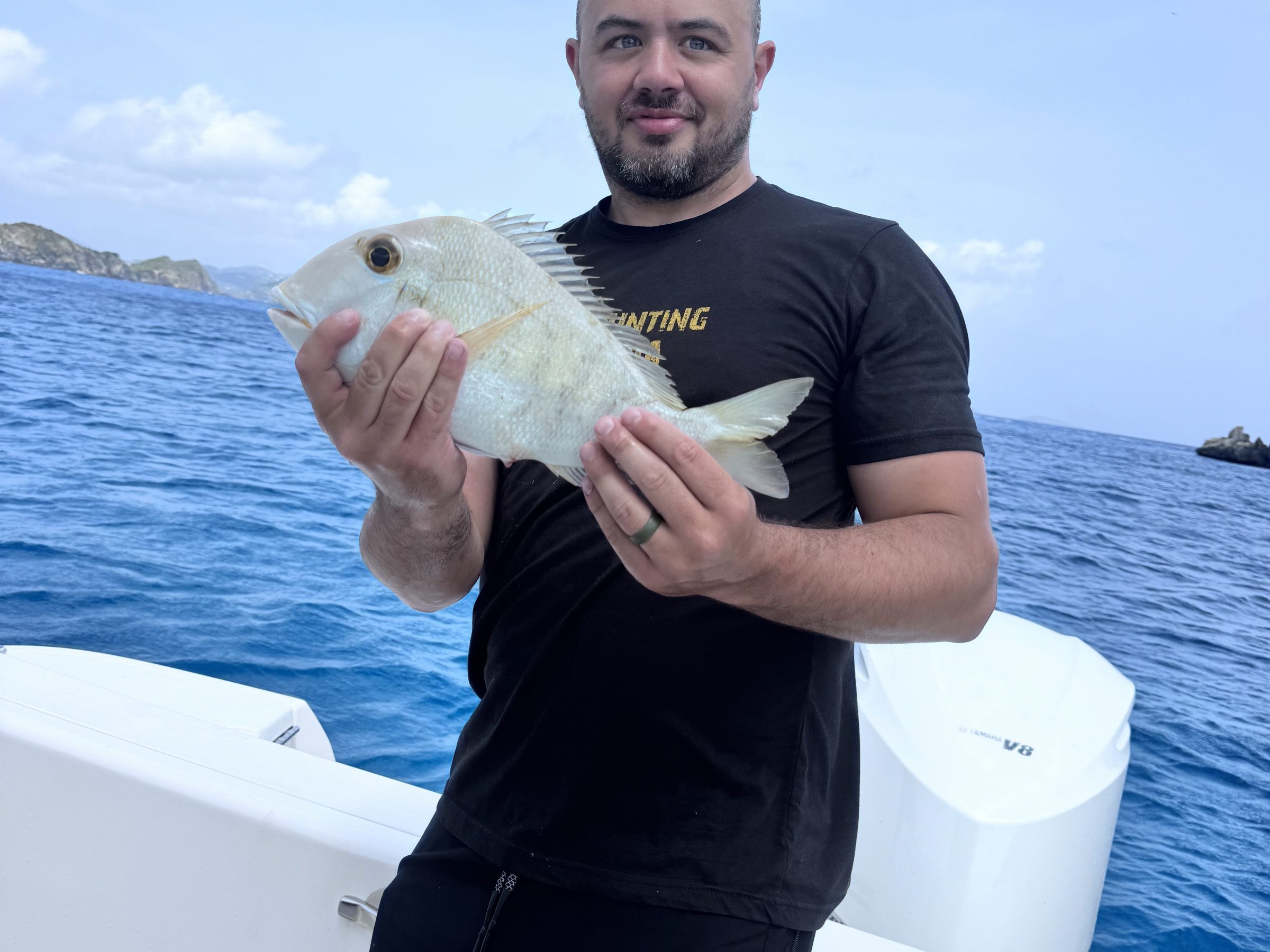 Man on boat holding a fish with ocean in background.
