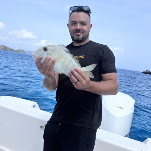 Man on boat holding a fish with ocean in background.