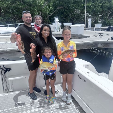 Five people on a boat holding fish, smiling.