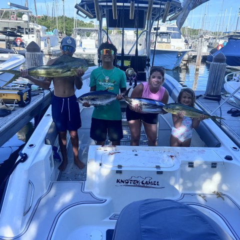Three kids on a boat displaying caught fish at a marina.