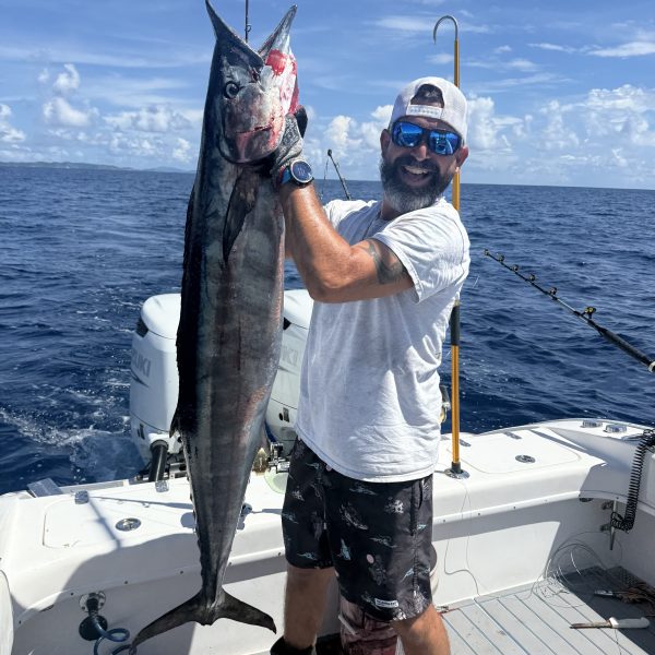Person on a boat holding a large fish with the ocean in the background.