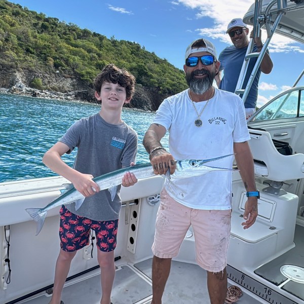 Boy and man hold a fish on a boat with ocean and hills in the background.