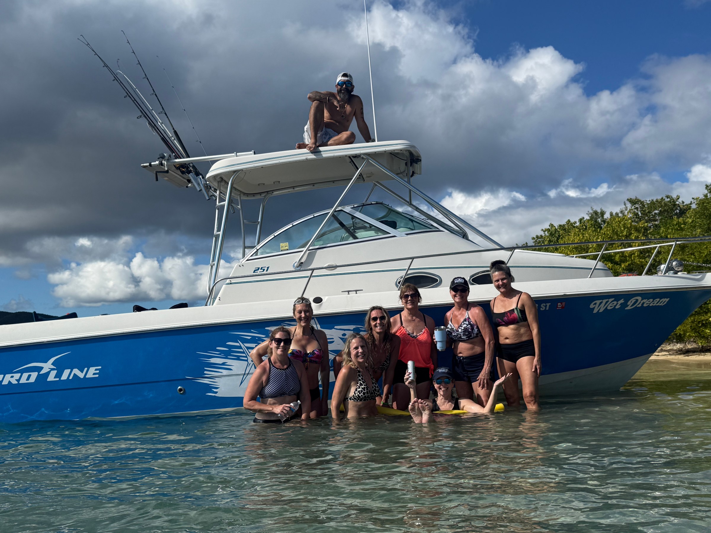 Group of people in water posing by a blue and white boat.