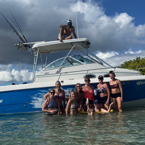 Group of people in water posing by a blue and white boat.