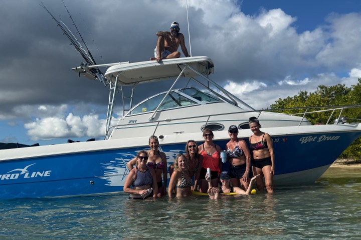 Group of people in water posing by a blue and white boat.