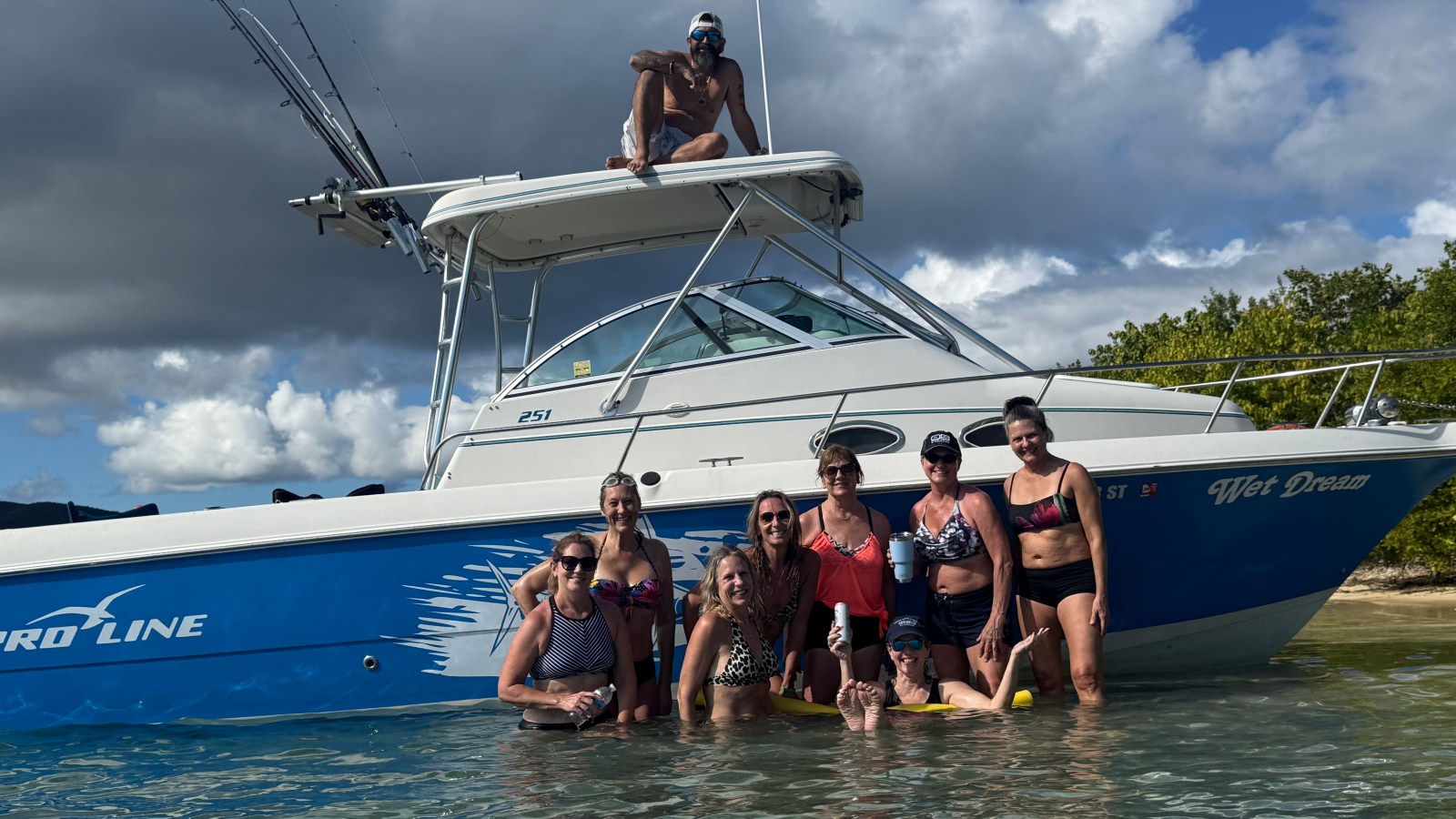 Group of people in water posing by a blue and white boat.