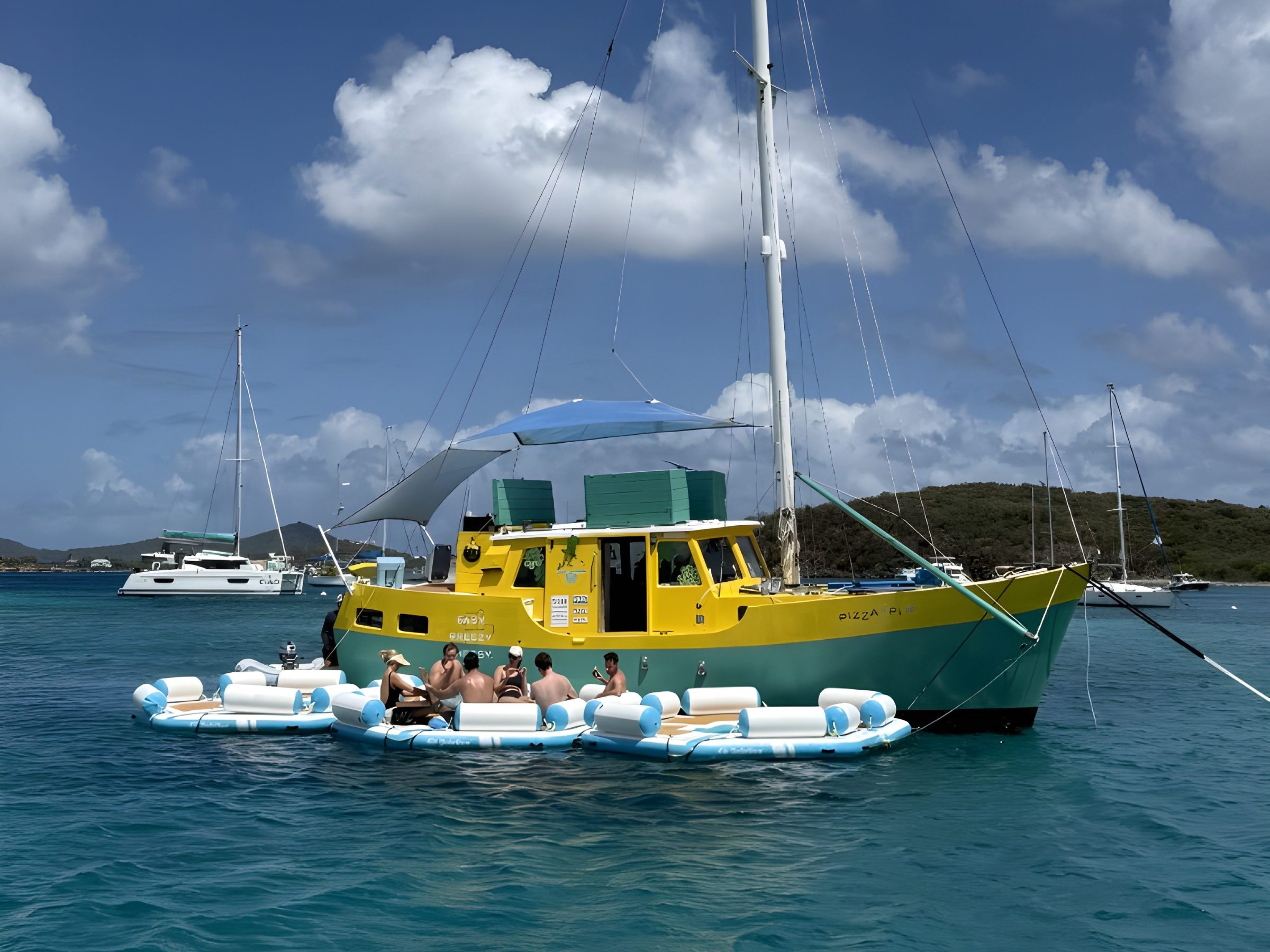 Yellow boat on blue water with people relaxing on floating inflatables.