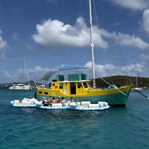 Yellow boat on blue water with people relaxing on floating inflatables.