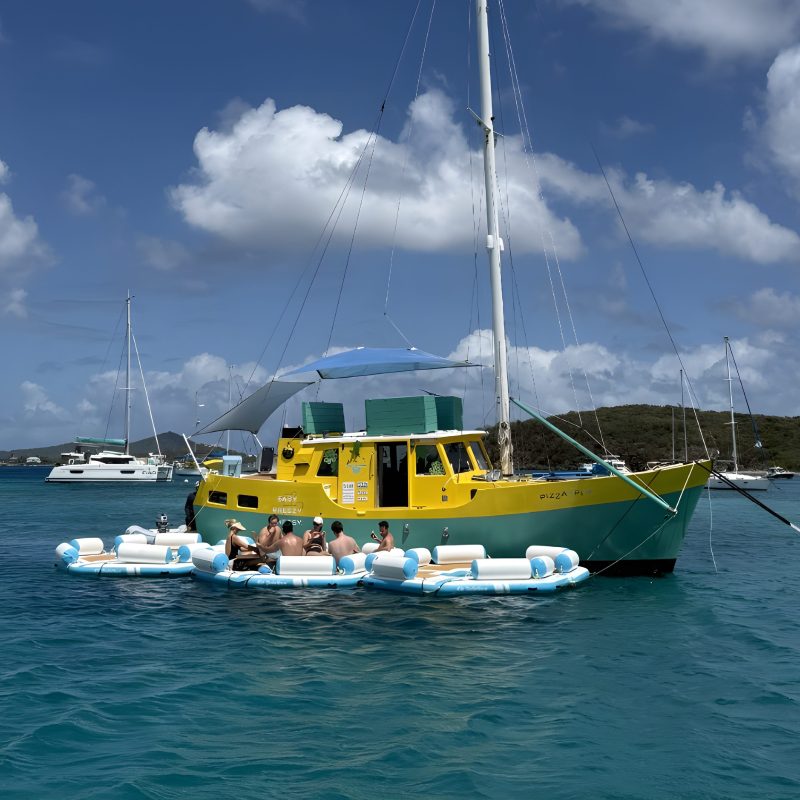 Yellow boat on blue water with people relaxing on floating inflatables.