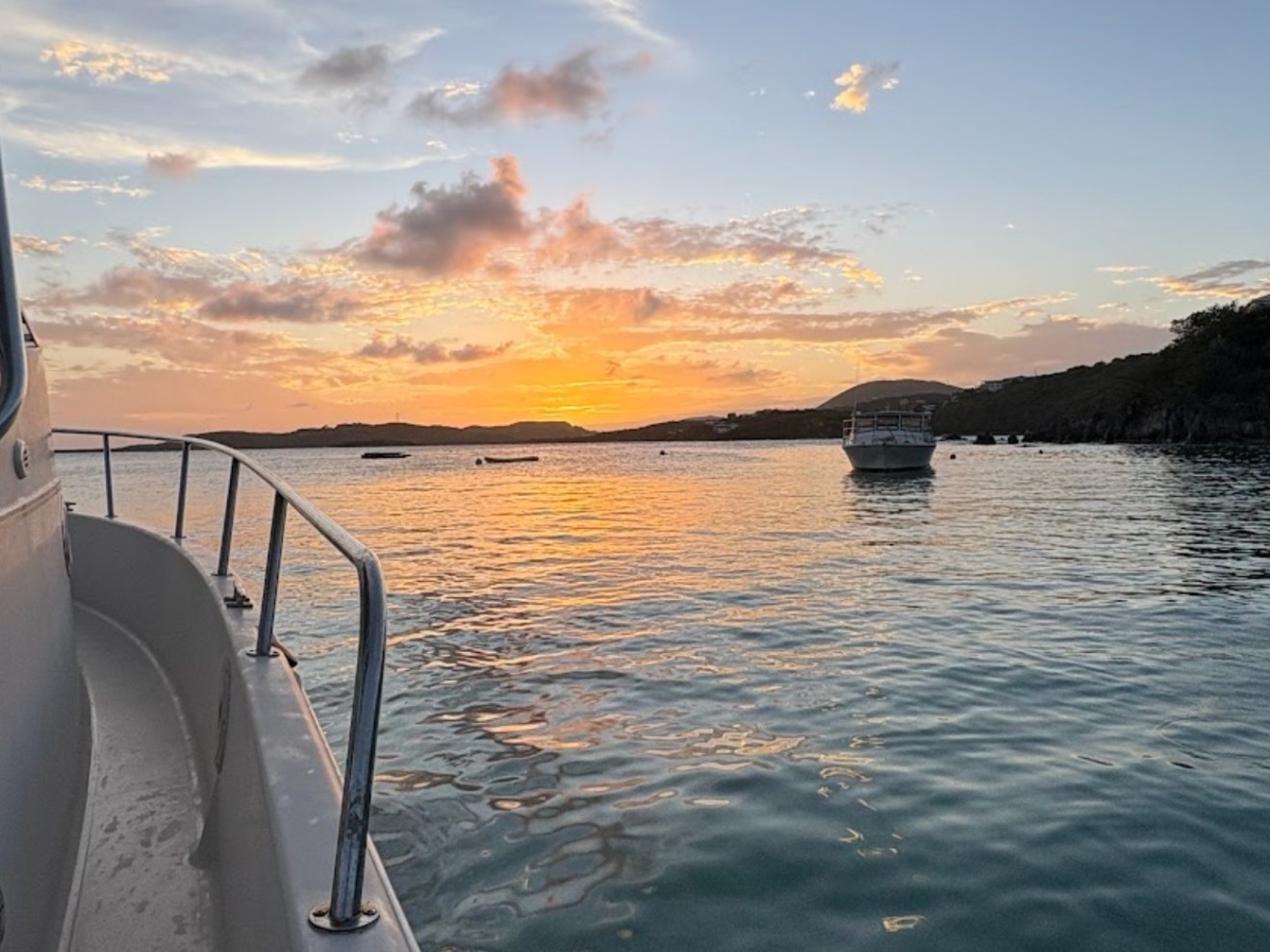 Sunset view from a boat on calm water with another boat in the distance.