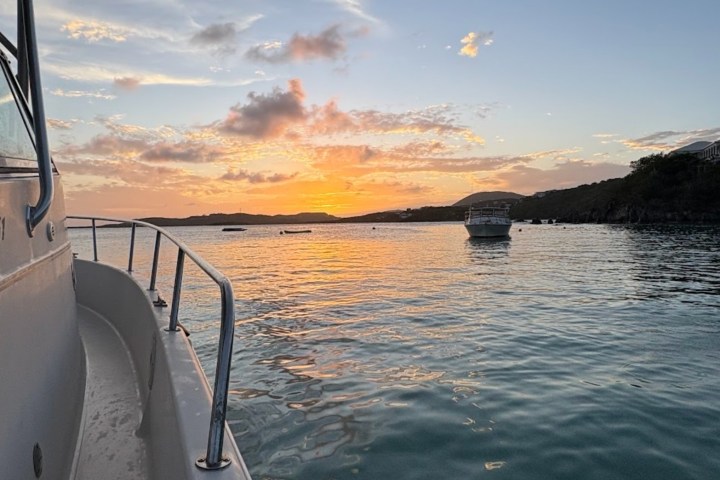 Sunset view from a boat on calm water with another boat in the distance.
