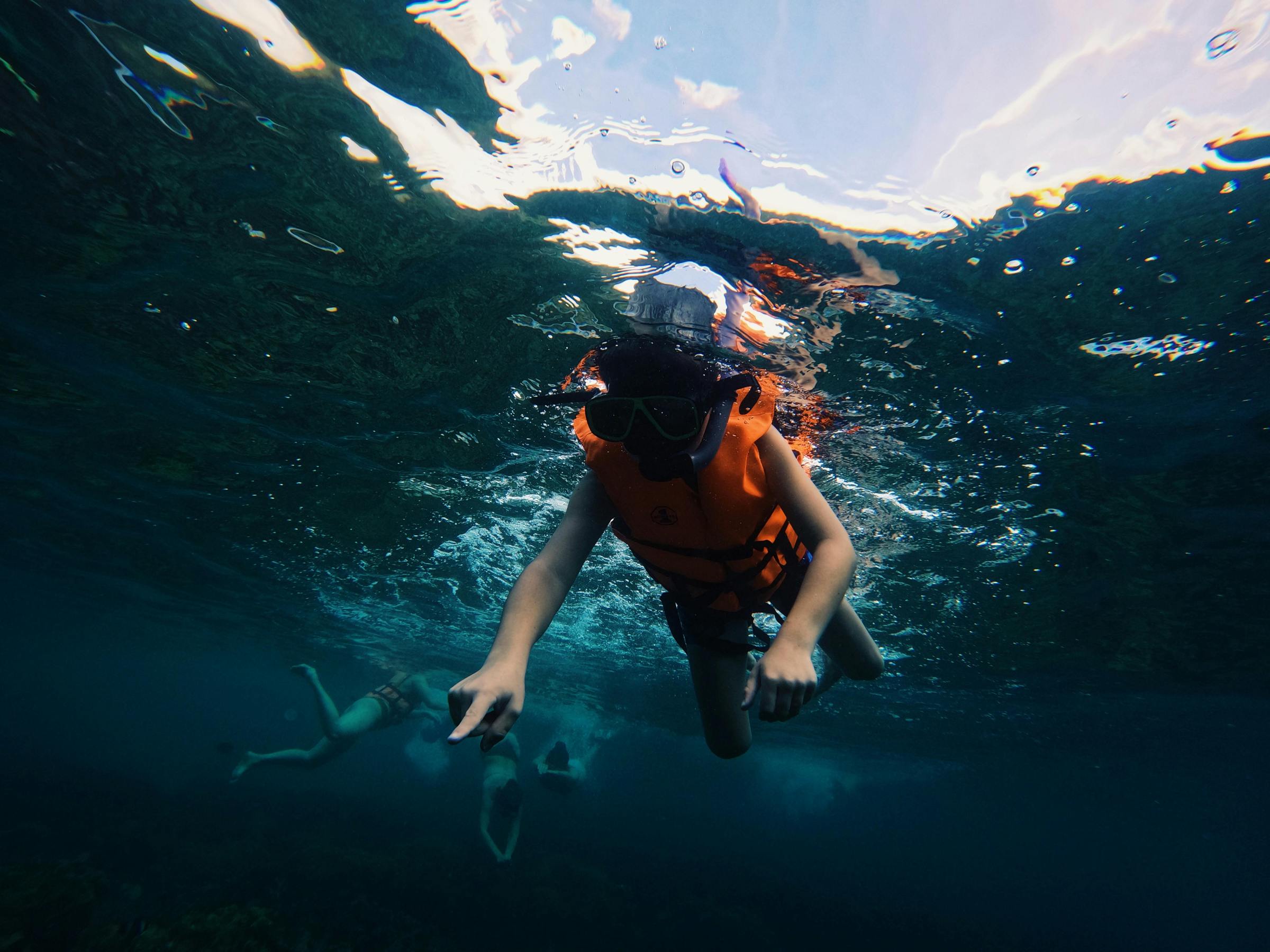 Person snorkeling underwater in a life jacket, with others visible in the background.