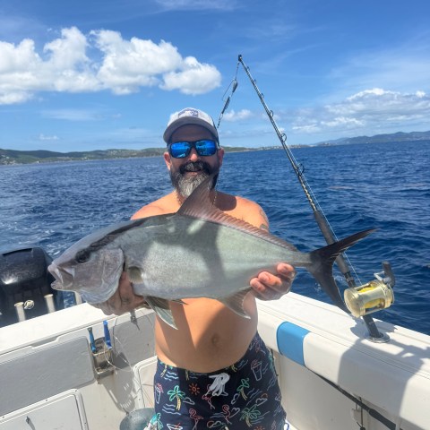 Man holding a large fish on a boat under a clear sky.